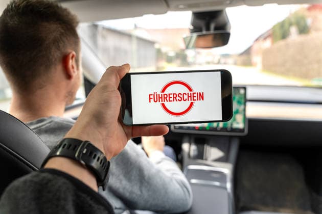 Ein Autofahrer hält ein Smartphone mit dem Hinweis Führerschein und steht für Änderungen im Verkehrsrecht. Das Bild symbolisiert neue Regeln, Vorschriften und Anpassungen rund um Fahrerlaubnis und Verkehrssicherheit.