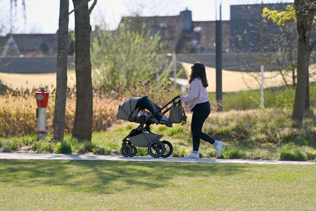 Frau schiebt Kinderwagen durch einen Park