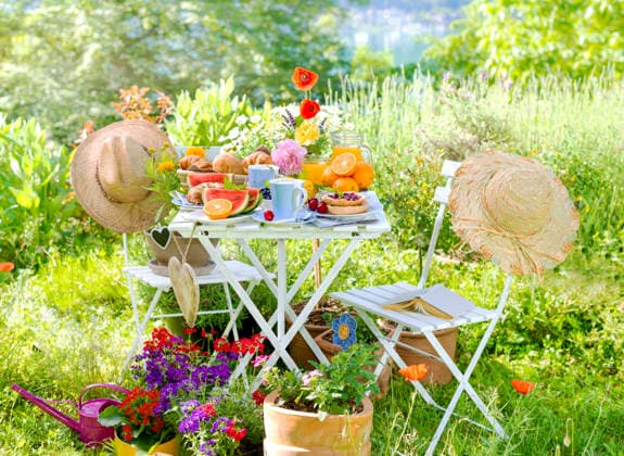 Fruehstueck fuer zwei, angerichtet auf einem Tisch im bunt bluehenden Garten am See mit Sonnenhueten und Herzen, Composing Breakfast for two, served on a table in a colorful garden blooming with coneflowers and hearts, Composing BLWS745584