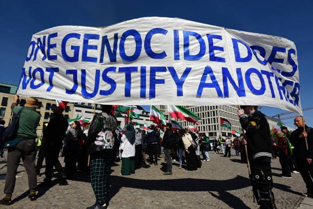 Gegner von Reza Pahlavi protestieren am Pariser Platz am Brandenburger Tor gegen den Besuch Pahlavis. Banner mit der Aufschrift One genocide does no justify another. Vor dem Reichstag versammelten sich zu selben Zeit Unterstützer Pahlavis. Protest gegen Reza Pahlavi