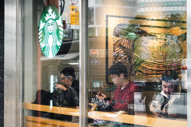 Besucher sitzen in einer Starbucks-Filiale und nutzen ihre Smartphones; das Cafe dient als Ort für Pause und alltägliche Freizeit