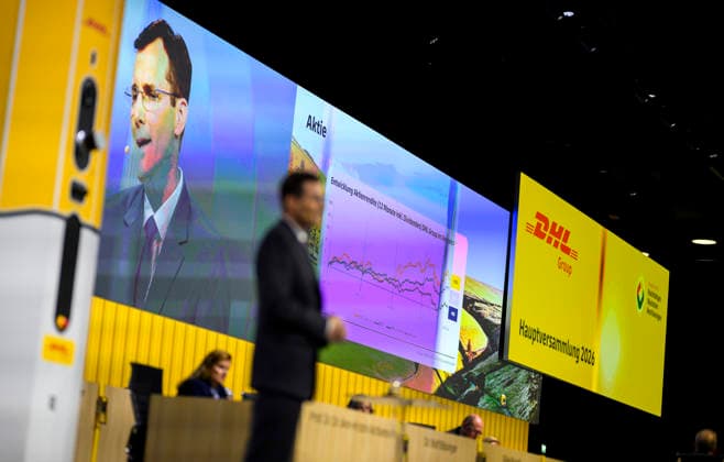 Feature, die Entwicklung der Aktie der DHL auf dem Screen, davor Tobias Meyer (CEO, Vorstandsvorsitzender) bei seiner Rede. Ordentliche Hauptversammlung der Deutsche Post AG, am 05.05.2026 in Bonn Deutschland. @ World Conference Center