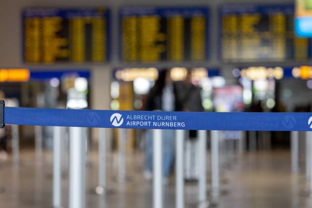 Eröffnung der neuen CT-Kontrollstelle am Airport Nürnberg, Nürnberg, 08.05.2026 Absperrband mit Logo des Albrecht Dürer Airport Nürnberg im Terminal. Im unscharfen Hintergrund sind Abflugtafeln und Bereiche des Flughafenbetriebs zu sehen. Nürnberg Bayern Deutschland