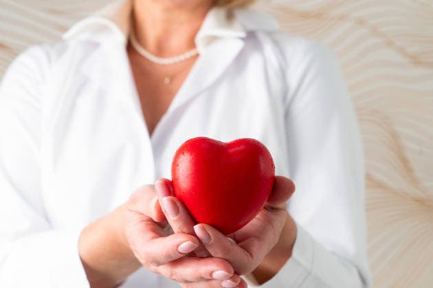 Eine mitfühlende Frau in einem weißen Laborkittel, die ein Herzsymbol in den Händen hält, das Fürsorge und Hingabe widerspiegelt A smiling woman dressed in a lab coat joyfully holds a bright red heart symbolizing care, love, and health (License=RF) ,model released, Symbolfoto Copyright: xZoonar.com AnastasyxYarmolovichx 25014667 ,model released, Symbolfoto ,property released