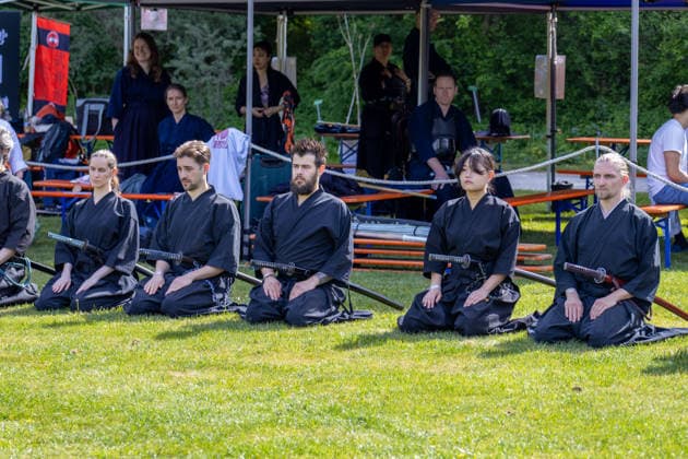 Teilnehmer einer japanischen Kampfkunstgruppe knien mit traditionellen Schwertern auf einer Wiese. Die Vorführung verbindet Disziplin, Meditation und Elemente der Samurai-Kultur mit asiatischer Schwertkunst. Traditionelles Japanisches Frühlingsfest im Botanischen Garten Augsburg. Das Event im Rahmen des 90-jährigen Garten-Jubiläums