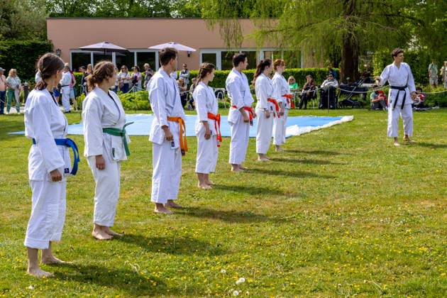 Karategruppe mit unterschiedlich farbigen Gürteln bei einem gemeinsamen Training im Freien. Die Teilnehmer üben Techniken und Bewegungsabläufe der japanischen Kampfkunst unter Anleitung eines Trainers. Traditionelles Japanisches Frühlingsfest im Botanischen Garten Augsburg. Das Event im Rahmen des 90-jährigen Garten-Jubiläums