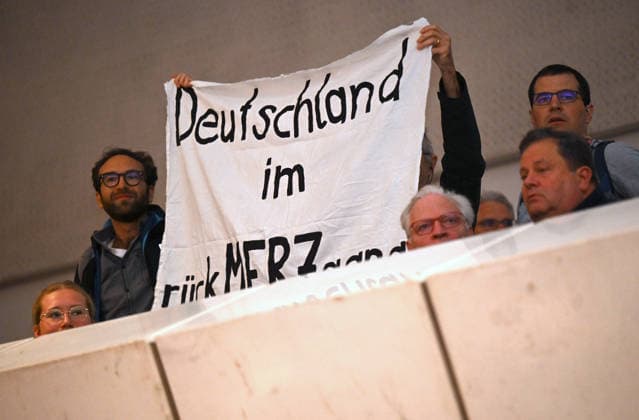 Proteste mit Banner Deutschland im rueckMERZgang bei einer Podiumsveranstaltung zum Thema Gemeinsam Zukunft gestalten mit Bundeskanzler Friedrich Merz (CDU) beim Katholikentag in Wuerzburg (im Foto vom 15.05.2026). Bis Sonntag werden beim 104. Deutschen Katholikentag unter dem biblischen Leitwort Hab Mut, steh auf! mehrere zehntausend Teilnehmende zu insgesamt 900 Veranstaltungen erwartet. Das Treffen soll angesichts von Krieg, Klimawandel, sozialer Spaltung sowie Vertrauenskrisen in Politik und Kirche dazu ermutigen, nach Wegen fuer die Zukunft zu suchen. (Siehe epd-Meldung vom 14.05.2026) EDITORIAL USE ONLY