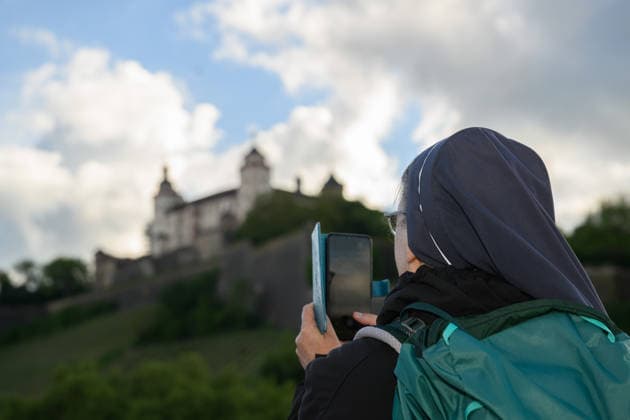 Eine Ordensschwester fotografiert die Festung Marienberg von der Alten Mainbruecke aus beim Katholikentag in Wuerzburg (Foto vom 15.05.2026). Bis Sonntag werden beim 104. Deutschen Katholikentag unter dem biblischen Leitwort Hab Mut, steh auf! mehrere zehntausend Teilnehmende zu insgesamt 900 Veranstaltungen erwartet. Das Treffen soll angesichts von Krieg, Klimawandel, sozialer Spaltung sowie Vertrauenskrisen in Politik und Kirche dazu ermutigen, nach Wegen fuer die Zukunft zu suchen. (Siehe epd-Meldung vom 15.05.2026) EDITORIAL USE ONLY