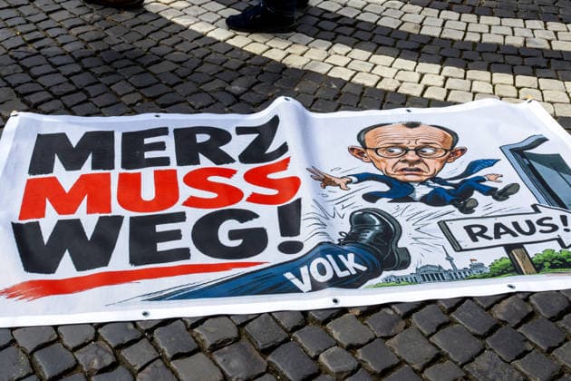 Demonstration gegen die aktuelle Bundesregierung unter Bundeskanzler Friedrich Merz in Augsburg. Unter dem Motto: Merz muss weg! Banner mit Aufschrift: MERZ MUSS WEG! Mit Illustration von einem Fuß auf dem VOLK steht und einer Illustration von Bundeskanzler Friedrich Merz (CDU) der durch eine Tür fliegt mit einem Schild mit Aufschrift: RAUS!