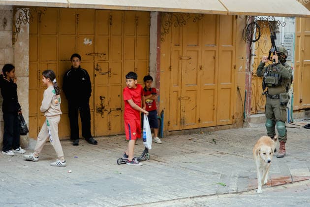 Hebron Israeli Settlers Tour May 16 An armed Israeli soldier stands guard near children standing by closed shop doors in the Old City of Hebron, the occupied West Bank, on May 16, 2026. The area is routinely secured by troops to allow Israeli settlers to tour the city. Hebron West Bank Palestinian Territories Copyright: xMosabxShawerx
