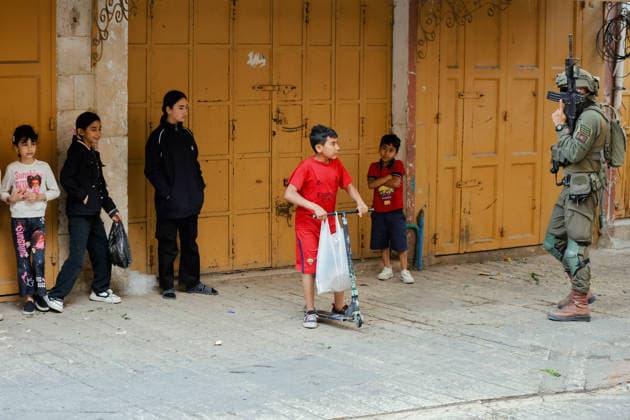 Hebron Israeli Settlers Tour May 16 An armed Israeli soldier stands guard near children standing by closed shop doors in the Old City of Hebron, the occupied West Bank, on May 16, 2026. The area is routinely secured by troops to allow Israeli settlers to tour the city. Hebron West Bank Palestinian Territories Copyright: xMosabxShawerx