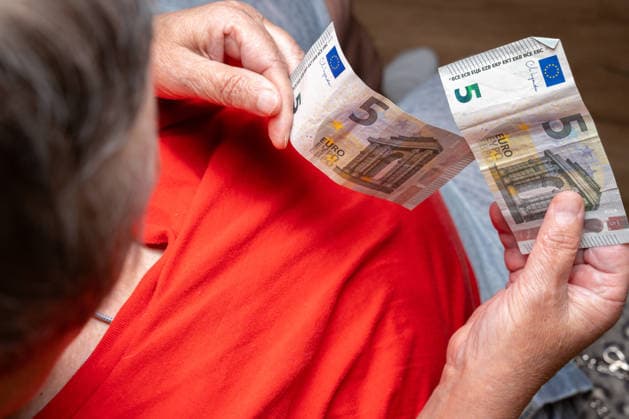 Eine korpulente Rentnerin zählt wenige Euroscheine mit ihren Händen. Das Bild symbolisiert finanzielle Unsicherheit, Altersarmut und den täglichen Kampf mit steigenden Preisen und knapper Rente.