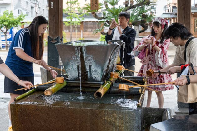 Besucher reinigen ihre Hände an einem traditionellen Wasserbecken im Kushida-Schrein in Fukuoka, Japan. Die Szene zeigt ein typisches Reinigungsritual vor dem Betreten des Schreins und vermittelt japanische Kultur, Tradition und religiöse Bräuche.