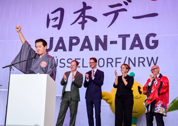 Japan-Tag 2026 in Düsseldorf, einzigartiges Kulturfest in der Landeshauptstadt von NRW - Takao Hariya, Präsident des japanischen Clubs in Düsslddorf bei seienr Begrüssungsrede - im Hitergrund stehen NRW Ministerpräsident Hendrik Wüst, NRW Ministerin für Wirtschaft und Kultur Mona Neubaur und der japanische Generalkonsul für Düsseldorf Yoshitaka Tsunoda überraschte die Zuschauer als bekennender Fan von Fortuna Düsseldorf - im Hintergrund Applaus von Düsseldorfs OB Dr. Stephan Keller, NRW Ministerpräsident Hendrik Wüst, NWR Wirtschafts & Kultur Ministerin Mona Neubaur und dem japanischen Generalkonsul für Düsseldorf Yoshotaka Tsunoda auf der Bühne... Düsseldorf Burgplatz NRW Deutschland