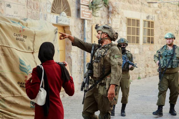 Hebron Israeli Settlers Tour May 23 An armed Israeli soldier gestures while speaking to a woman next to a storefront in the Old City of Hebron, in the occupied West Bank, on May 23, 2026. The area is routinely secured by military forces to escort settlers touring the city, amid ongoing tensions regarding settlement expansion near the Ibrahimi Mosque. Hebron West Bank Palestinian Territories Copyright: xMosabxShawerx