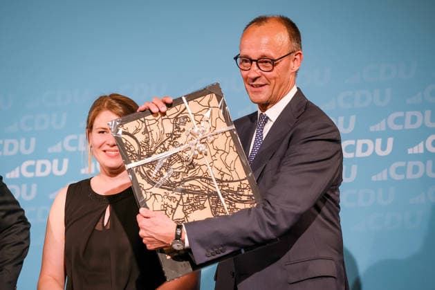 27.05.2026, Politik, Bundeskanzler Friedrich Merz (CDU) bekommt ein Geschenk - das Stadtblid - zu Gast als Festredner beim Festakt in der Schützenhalle Hüsten bei Arnsberg. 80 Jahre Neheim-Hüstener Programm. Nordrhein-Westfalen Deutschland