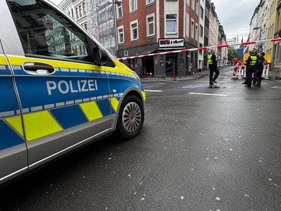 Polizeiwagen vor einer abgesperrten Straße am Friesenwall in Köln. Mehrere Polizisten stehen hinter einer rot-weißen Absperrung vor der Bar mit angeschaltetem Warnblinker.