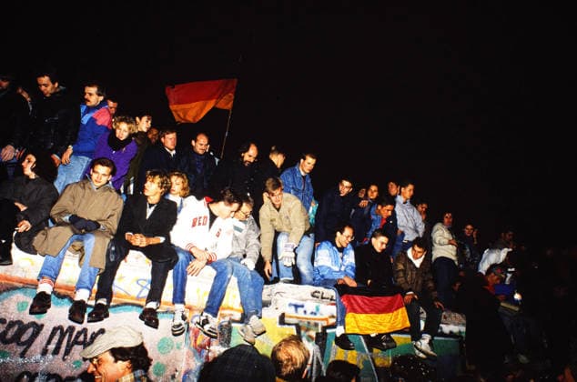 Junge Menschen sitzen nachts auf der Berliner Mauer am Potsdamer Platz, einige halten Deutschlandfahnen, die Mauer ist mit Graffiti bemalt, Deutschland, 1989. Berlin Berlin Deutschland Copyright: xUnitedxArchivesx xSvenxSimonxArchive