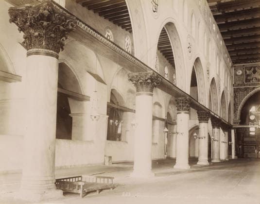 RECORD DATE NOT STATED Jerusalem. Mosquà e el-Aksa, - intà rieur, Interior of the Al-Aqsa Mosque on the Temple Mount in Jerusalem, photograph, Part of Travel album with photos of Jerusalem and other biblical places., inscription: BFK Rives , negative number: 283 , photographer: Maison Bonfils, Jerusalem, c. 1867 - c. 1895, pasteboard, paper, albumen print, height 225 mm x width 282 mm, temple, shrine, Islam, Mohammedanism, Al-Aqsa Mosque, A long interior view showing a row of tall cylindrical columns with ornate carved capitals supporting a decorated horizontal beam and a high ceiling with exposed wooden beams, a series of arched openings along the wall each topped by small circular windows, hanging pendant lights suspended from the ceiling at various heights, Copyright Penta Springs LCK260531_03384
