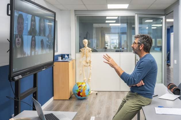 Der Lehrer leitet den virtuellen Anatomieunterricht von einem Labor aus und erklärt Skelettstrukturen neben einem menschlichen Skelett, während er mit den Schülern über eine Großbildvideokonferenz für E Learning interagiert Teacher leads virtual anatomy class from a lab, explaining skeletal structures beside a human skeleton while interacting with students via large screen video conference for e learning Copyright: imageBROKER UnaixHuizi ibxuhu18092344.jpg ,model released, Symbolfoto ,property released