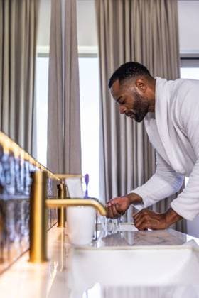 Senior African American man in bathrobe washing hands at bathroom sink with gold faucet, copy space, model released, property released, 27.01.2026 06:00:00, 10615960 Copyright: xIDS-260626_1xcreatorid:x0x 10615960