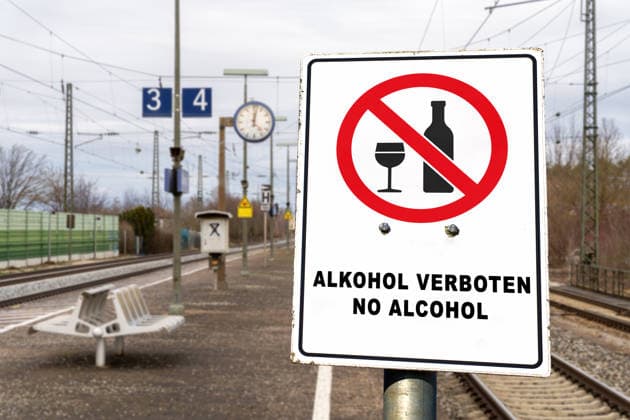 FOTOMONTAGE, Schild am Bahnhof: ALKOHOL VERBOTEN, NO ALCOHOL. Die Deutsche Bahn (DB) führt schrittweise ein bundesweites Alkoholkonsumverbot an ihren Bahnhöfen ein. Das Verbot gilt für Bahnsteige und Bahnhofshallen, nicht jedoch für gastronomische Betriebe