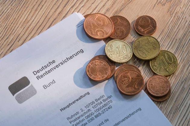 Nahaufnahme eines Briefkopfes der Deutschen Rentenversicherung Bund auf einem Holzuntergrund, auf dem eine kleine Ansammlung von Euro-Cent-Münzen (Kupfergeld und Messingmünzen) liegt.