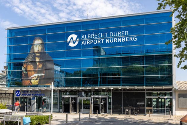 Baustart Cargo ‹Center 3 am Flughafen Nürnberg, Nürnberg, 04.08.2026 Das Terminalgebäude des Albrecht Dürer Airport Nürnberg zeigt ein großformatiges Porträt von Albrecht Dürer an der Fassade. Der Flughafen erweitert seinen Cargo-Bereich und startet den Bau des neuen Cargo Centers 3 (CCN 3), um der anhaltend hohen Nachfrage nach Logistikflächen gerecht zu werden. Nürnberg Flughafen Bayern Deutschland