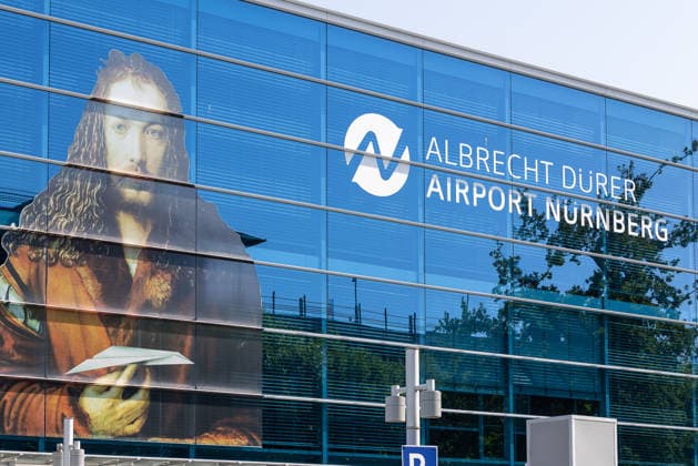 Flughafen Nürnberg, 04.08.2026 Fassade des Albrecht Dürer Airport Nürnberg mit großformatigem Selbstbildnis von Albrecht Dürer und Logo des Flughafens. Die Glasfassade des Terminalgebäudes spiegelt den blauen Himmel. Nürnberg Flughafen Bayern Deutschland