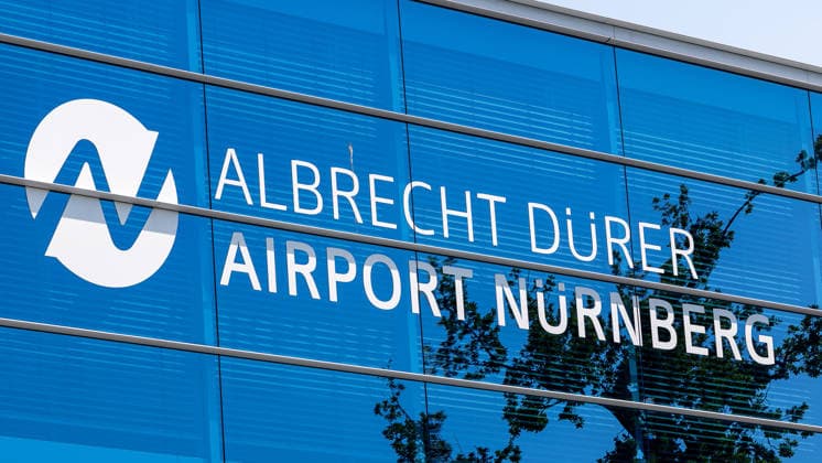Flughafen Nürnberg, 04.08.2026 Schriftzug und Logo des Albrecht-Dürer-Airport Nürnberg an der Fassade des Terminalgebäudes. Die blaue Glasfront spiegelt Bäume und Himmel wider. Nürnberg Flughafen Bayern Deutschland