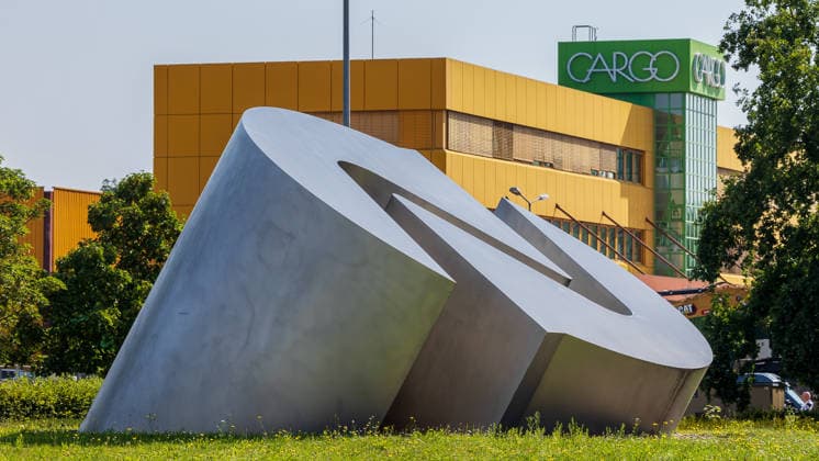Baustart Cargo ‹Center 3 am Flughafen Nürnberg, Nürnberg, 04.08.2026 Eine markante Metallskulptur des Flughafen Logo steht im Vordergrund des Geländes, auf dem der Bau des neuen Cargo Center 3 am Flughafen Nürnberg beginnt. Im Hintergrund ist die Fassade eines bestehenden Cargo-Center 1 mit dem Schriftzug Cargo zu erkennen. Nürnberg Flughafen Bayern Deutschland