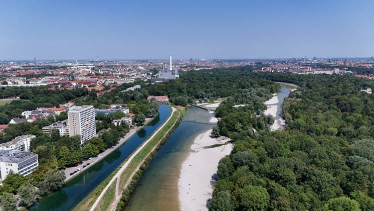 Ein Sommertag in der Landeshauptstadt München. Hier der Blick auf die auf die Isar und den Isar Werkskanal (li.) sowie den Flaucher, Badegelände, Kiesstrand, sowie die Skyline der Stadt München mit Blick Richtung Norden, Stadtblick, Häusermeer, Erholungsgebiet, Sonnen, baden, Abkühlen