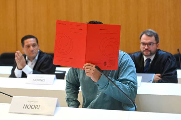 Der Angeklagte im Verhandlungssaal, verbirgt sein Gesicht hinter einem Schnellhefter. Hinten seine Anwaelte,Verteidiger. Urteil im Strafverfahren gegen Farhad Noori wegen Mordes u.a.(Seidlstrasse) am 06.08.2026 vor dem Oberlandesgericht Muenchen