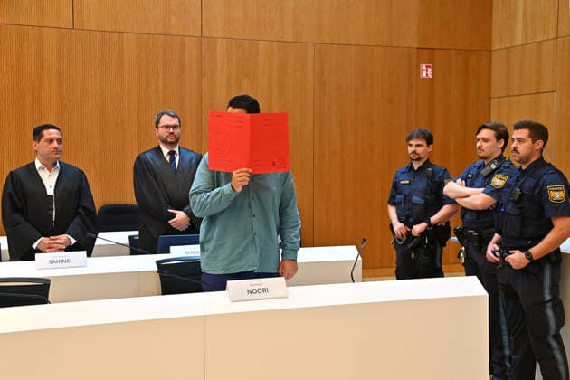 Der Angeklagte im Verhandlungssaal, verbirgt sein Gesicht hinter einem Schnellhefter.Hinten:seine Verteidiger RA Oemer SAHINCI, RA Johann BUND. Urteil im Strafverfahren gegen Farhad Noori wegen Mordes u.a.(Seidlstrasse) am 06.08.2026 vor dem Oberlandesgericht Muenchen