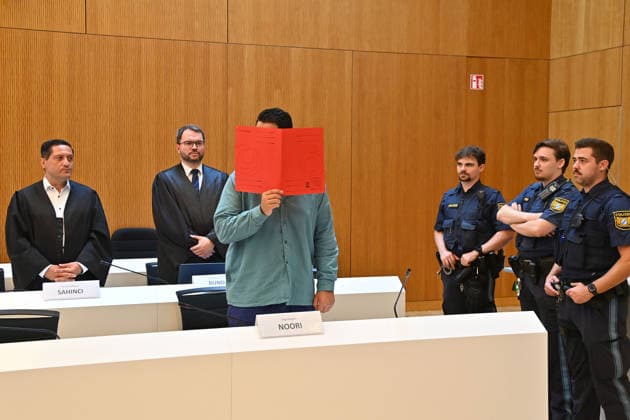 Der Angeklagte im Verhandlungssaal, verbirgt sein Gesicht hinter einem Schnellhefter.Hinten:seine Verteidiger RA Oemer SAHINCI, RA Johann BUND. Urteil im Strafverfahren gegen Farhad Noori wegen Mordes u.a.(Seidlstrasse) am 06.08.2026 vor dem Oberlandesgericht Muenchen