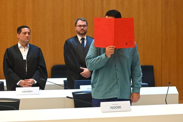 Der Angeklagte im Verhandlungssaal, verbirgt sein Gesicht hinter einem Schnellhefter.Hinten:seine Verteidiger RA Oemer SAHINCI, RA Johann BUND. Urteil im Strafverfahren gegen Farhad Noori wegen Mordes u.a.(Seidlstrasse) am 06.08.2026 vor dem Oberlandesgericht Muenchen