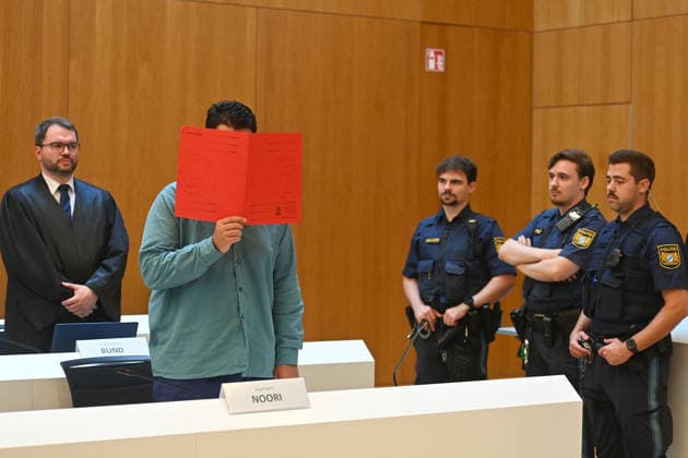 Der Angeklagte im Verhandlungssaal, verbirgt sein Gesicht hinter einem Schnellhefter.Hinten: seinVerteidiger RA Johann BUND. Urteil im Strafverfahren gegen Farhad Noori wegen Mordes u.a.(Seidlstrasse) am 06.08.2026 vor dem Oberlandesgericht Muenchen