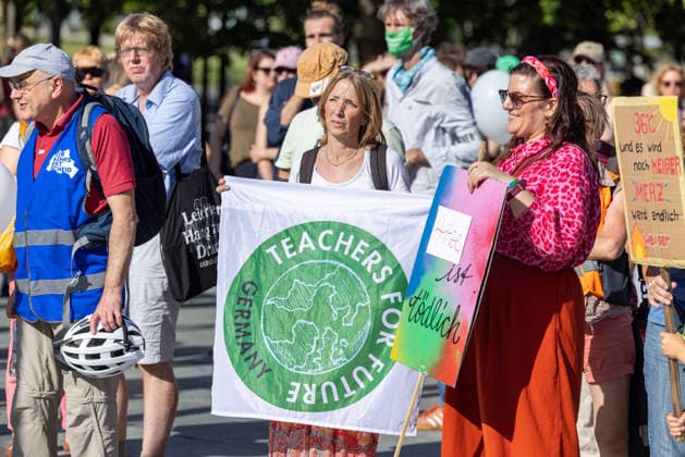 Fridays for Future Berlin - Hitzedemo. Deutschland, Berlin am 6. August 2026: Vor dem Kanzleramt protestieren Klimaaktivistinnen und Klimaaktivisten unter dem Motto Klimakrise eskaliert, Kanzler schweigt?!. Sie verlangen verstärkte Klimaschutzmaßnahmen, einen schnellen politischen Hitzeschutz sowie einen konsequenten Ausstieg aus fossilen Energien. Eine Frau hält Banner Teachers for Future Germany