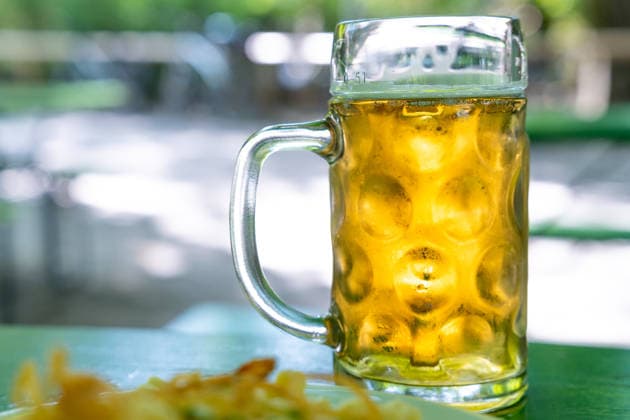 Zwei Maßkrüge Bier und eine Brotzeit (Käsespatzen) auf einem Tisch im Biergarten. Das Bild steht für bayerische Biergartenkultur, Geselligkeit und traditionelle Gastronomie in München und Bayern.