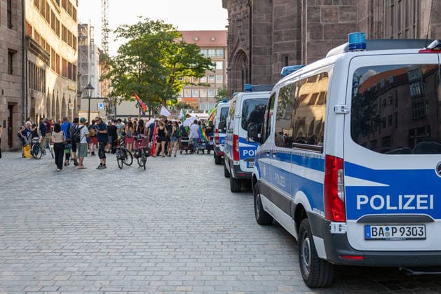 Polizeieinsatz bei Montagsdemo von Team Menschenrechte und Gegenprotesten, Nürnberg, 10.087.2026 Mehrere Einsatzfahrzeuge der Polizei stehen an der östlichen Seite der Lorenzkirche, während sich eine Gruppe von Demonstranten mit Fahnen und Transparenten versammelt. Passanten mit Fahrrädern beobachten das Geschehen auf dem Kopfsteinpflaster. Nürnberg Bayern Deutschland