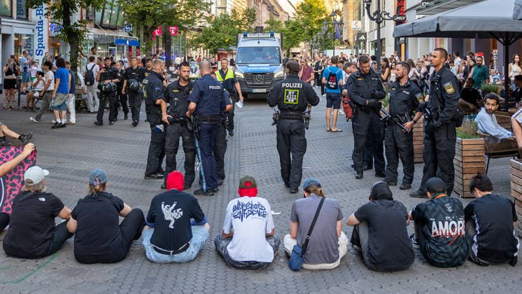 Polizeieinsatz bei Montagsdemo von Team Menschenrechte und Gegenprotesten, Nürnberg, 10.087.2026 In der Karolinenstraße blockiert eine Gruppe von Gegendemonstranten sitzend den Demonstrationszug von Team Menschenrechte . Zahlreiche Polizeibeamte in Einsatzkleidung stehen zwischen den Sitzenden und den Passanten, im Hintergrund ein Einsatzfahrzeug der Polizei. Nürnberg Bayern Deutschland