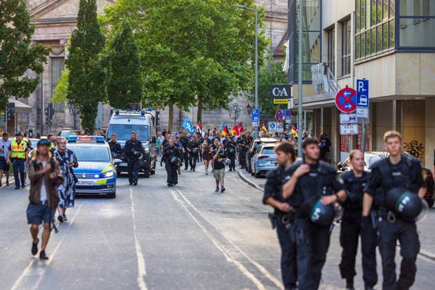 Polizeieinsatz bei Montagsdemo von Team Menschenrechte und Gegenprotesten, Nürnberg, 10.087.2026 Polizeikräfte in Schutzausrüstung begleiten einen Demonstrationszug mit Fahnen durch eine Innenstadtstraße. Fahrzeuge der Polizei sichern den Aufzug, während Passanten das Geschehen vom Straßenrand aus beobachten. Nürnberg Bayern Deutschland
