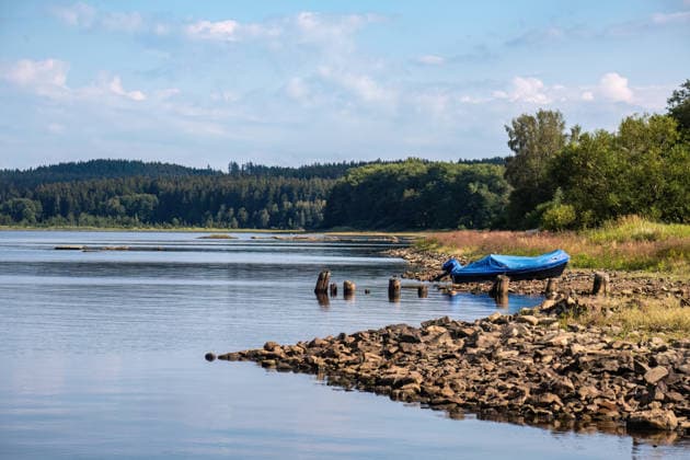Panoramablick über den Lipno-See mit ruhigem Wasser und blauem Sommerhimmel in Südböhmen, Tschechien Peaceful shoreline view across Lake Lipno with calm reflections, rocky coast and blue summer sky in South Bohemia. (License=RF) Copyright: xZoonar.com AnnabellxGsödlx 25410036