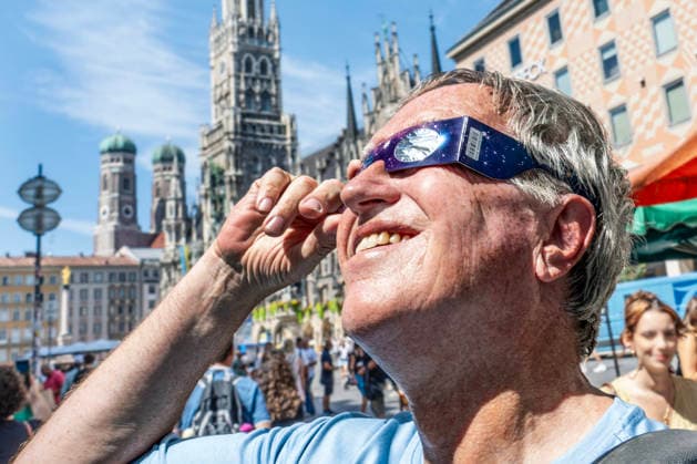 Sonnenfinsternis Brille, stolzer Besitzer einer Schutzbrille auf dem Marienplatz, Brillen sind leider fast überall ausverkauft, riesige Nachfrage wegen der partiellen Sonnenfinsternis morgen Abend, München, 11. August 2026 Deutschland, München, 11. August 2026, Sonnenfinsternis Brille, stolzer Besitzer einer Schutzbrille, schaut auf dem Marienplatz in die Sonne, Mann hat eine der letzten Exemplare im Deutsches Museum Shop am Rindermarkt erstanden, halbe Stunde in einer langen Schlange dafür angestanden, Sonnen-Sicht-Brille kostete nur 3,95 Euro, Brillen sind leider fast überall ausverkauft, riesige Nachfrage wegen der partiellen Sonnenfinsternis morgen Abend, als Augenschutz braucht man eine spezielle Sonnenfinsternisbrille mit CE-Ken