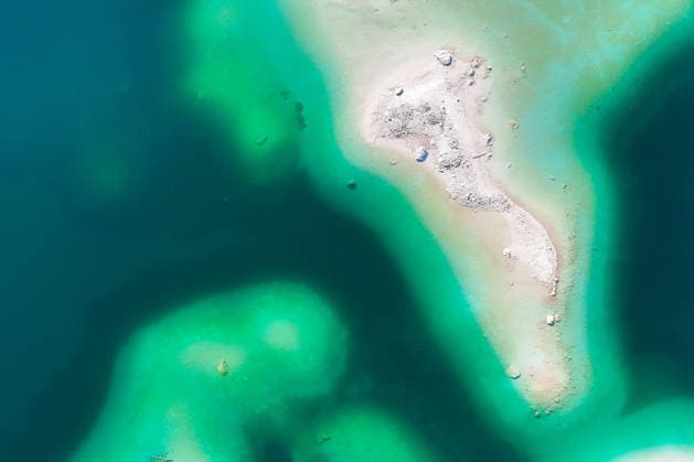 Wetterfeature, Morgenstille am Eibsee: Unterhalb der Zugspitze liegt der See bei Grainau nahe Garmisch-Partenkirchen in den frühen Stunden noch ruhig und nahezu unberührt. Doch an heißen Sommertagen ändert sich das Bild häufig schon ab Mittag. Dann strömen zahlreiche Ausflügler und Urlauber an den durch soziale Medien weltweit bekannt gewordenen Bergsee. Der zunehmende Massentourismus sorgt regelmäßig für einen regelrechten Besucheransturm. Unter dem hohen Verkehrsaufkommen, zugeparkten Straßen und dem großen Andrang leiden zunehmend auch die Anwohner in Grainau und rund um den Eibsee. (Aufnahme mit einer Drohne) Grainau Bayern Deutschland Grainau