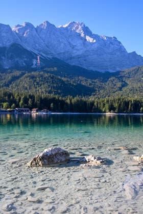 Wetterfeature, Morgenstille am Eibsee: Unterhalb der Zugspitze liegt der See bei Grainau nahe Garmisch-Partenkirchen in den frühen Stunden noch ruhig und nahezu unberührt. Doch an heißen Sommertagen ändert sich das Bild häufig schon ab Mittag. Dann strömen zahlreiche Ausflügler und Urlauber an den durch soziale Medien weltweit bekannt gewordenen Bergsee. Der zunehmende Massentourismus sorgt regelmäßig für einen regelrechten Besucheransturm. Unter dem hohen Verkehrsaufkommen, zugeparkten Straßen und dem großen Andrang leiden zunehmend auch die Anwohner in Grainau und rund um den Eibsee. Grainau Bayern Deutschland Grainau