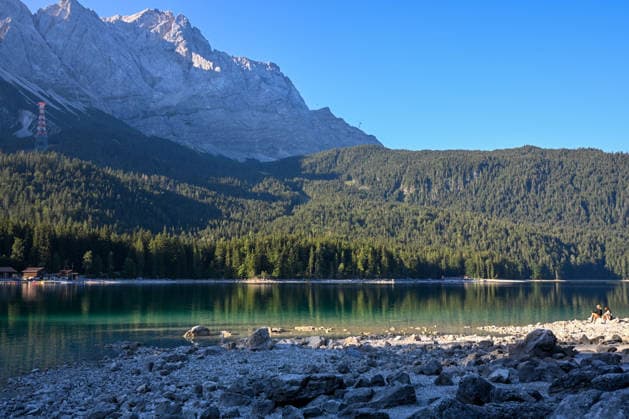 Wetterfeature, Morgenstille am Eibsee: Unterhalb der Zugspitze liegt der See bei Grainau nahe Garmisch-Partenkirchen in den frühen Stunden noch ruhig und nahezu unberührt. Doch an heißen Sommertagen ändert sich das Bild häufig schon ab Mittag. Dann strömen zahlreiche Ausflügler und Urlauber an den durch soziale Medien weltweit bekannt gewordenen Bergsee. Der zunehmende Massentourismus sorgt regelmäßig für einen regelrechten Besucheransturm. Unter dem hohen Verkehrsaufkommen, zugeparkten Straßen und dem großen Andrang leiden zunehmend auch die Anwohner in Grainau und rund um den Eibsee. Grainau Bayern Deutschland Grainau