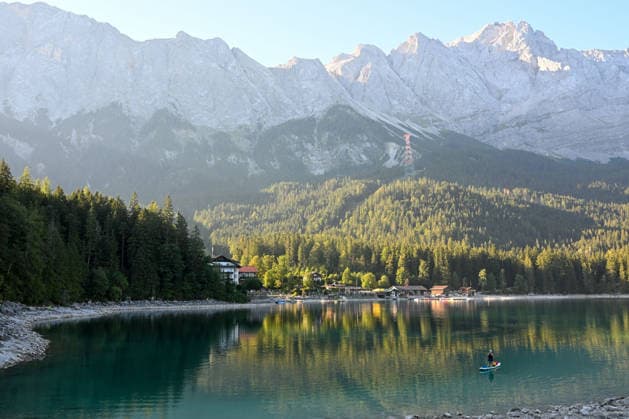 Wetterfeature, Morgenstille am Eibsee: Unterhalb der Zugspitze liegt der See bei Grainau nahe Garmisch-Partenkirchen in den frühen Stunden noch ruhig und nahezu unberührt. Doch an heißen Sommertagen ändert sich das Bild häufig schon ab Mittag. Dann strömen zahlreiche Ausflügler und Urlauber an den durch soziale Medien weltweit bekannt gewordenen Bergsee. Der zunehmende Massentourismus sorgt regelmäßig für einen regelrechten Besucheransturm. Unter dem hohen Verkehrsaufkommen, zugeparkten Straßen und dem großen Andrang leiden zunehmend auch die Anwohner in Grainau und rund um den Eibsee. Grainau Bayern Deutschland Grainau
