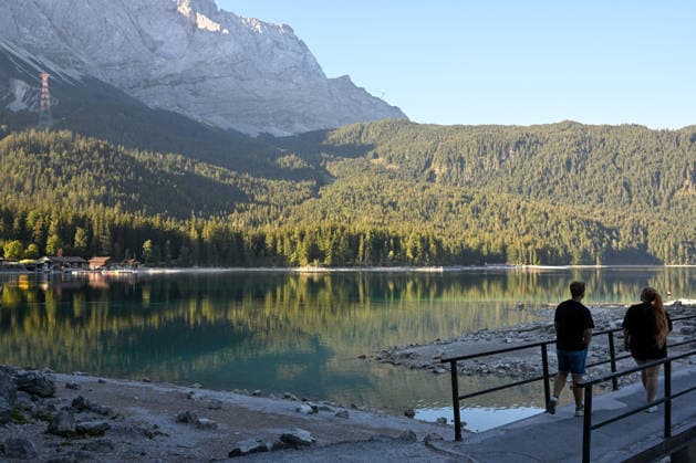 Wetterfeature, Morgenstille am Eibsee: Unterhalb der Zugspitze liegt der See bei Grainau nahe Garmisch-Partenkirchen in den frühen Stunden noch ruhig und nahezu unberührt. Doch an heißen Sommertagen ändert sich das Bild häufig schon ab Mittag. Dann strömen zahlreiche Ausflügler und Urlauber an den durch soziale Medien weltweit bekannt gewordenen Bergsee. Der zunehmende Massentourismus sorgt regelmäßig für einen regelrechten Besucheransturm. Unter dem hohen Verkehrsaufkommen, zugeparkten Straßen und dem großen Andrang leiden zunehmend auch die Anwohner in Grainau und rund um den Eibsee. Grainau Bayern Deutschland Grainau