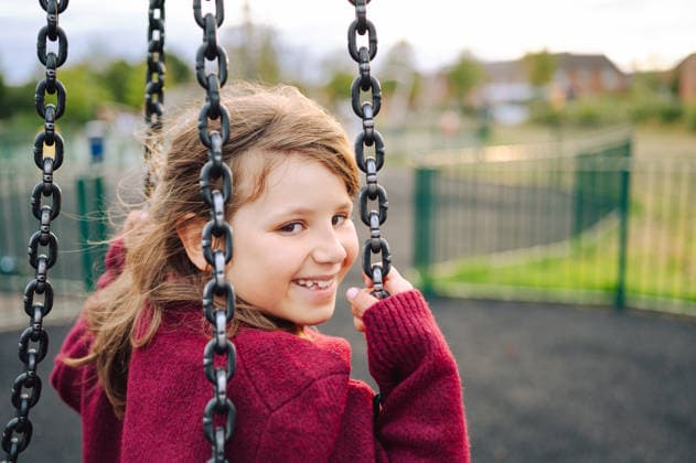 Happy young girl smiling while on a playground swing set Corby, England, United Kingdom CR_JNDO260908B7-2120816-01 ,model released, Symbolfoto ,property released